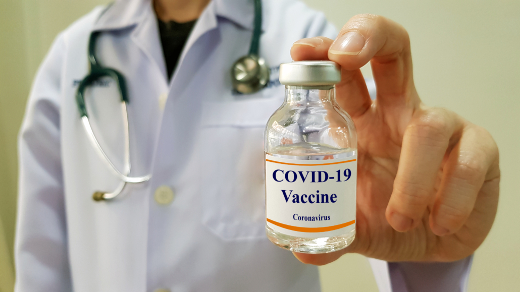 Image of person in labcoat holding a vaccine vial labeled COVID-19